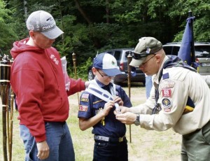 A scout leader helps a new Cub Scout don his new neckerchief and slide during a recent ceremony.